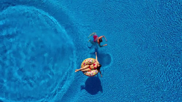 Aerial view of man dives into the the pool while girl is lying on a donut pool float