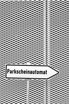 Ein Richtungszeichen mit dem Hinweis eines Parkscheinautomaten vor einer Streckmetall Fassade...