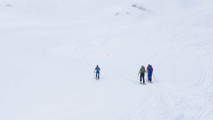 Fototapeta na wymiar Ski resort. Three tourists walking upwards by the ski in a mountains