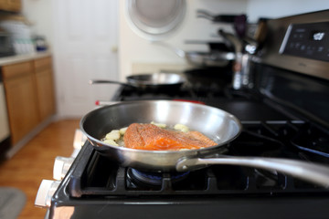 Steelhead frying in a stainless steel pan with the skin side down.