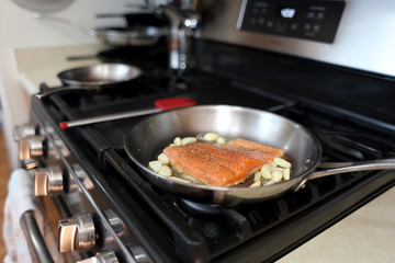 Steelhead frying in a stainless steel pan with the skin side down.