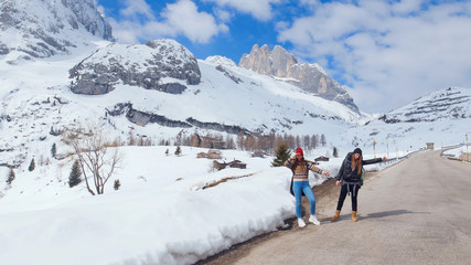 Fototapeta na wymiar Two young women traveling on the road in Dolomites with big backpack and guitar