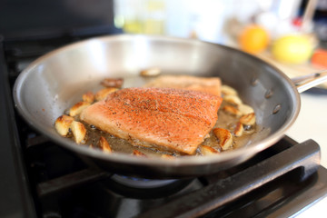 Steelhead frying in a stainless steel pan with the skin side down.