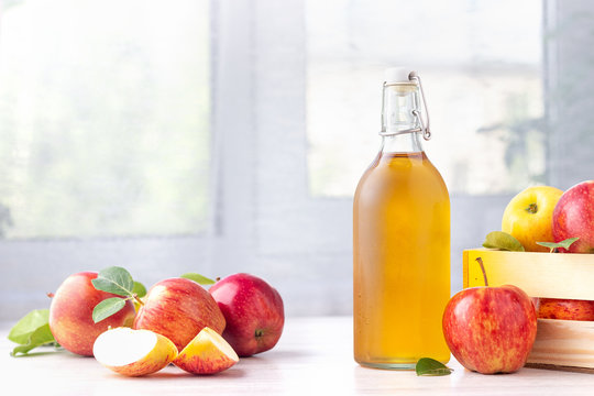 Healthy organic food. Apple cider vinegar in glass bottle and fresh red apples on a light background.