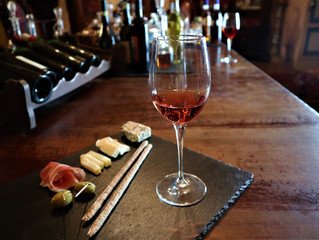 Glass of red wine,  olives, prosciutto, salami, aged cheese on a table at a cozy  bar.