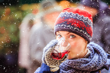 Enjoying Christmas time on the Christmas market. Young girl is drinking mulled wine.