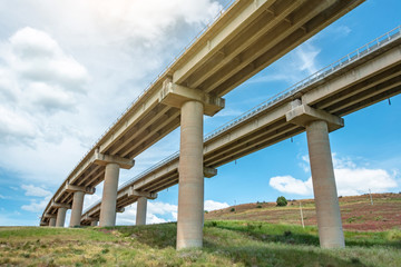 Two road turn highway bridge, viaduct supports in the valley among the green hills, transport infrastructure.
