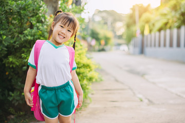 Happy student kids waiting for school bus with her bag on the side of the road. Concept for education open semester and back to school.