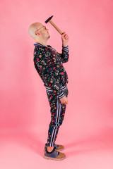 Funny fashionable man with hammer in his hand striking his head on pink background.