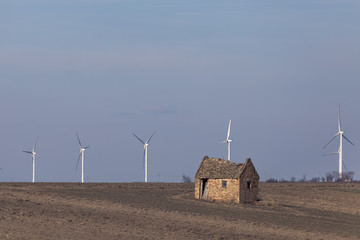 Old ruined house on agricultural ground with wind warm in background