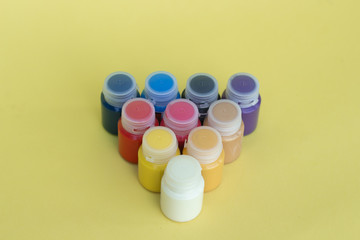 Multicolored plastic cans with acrylic paint on a yellow background. Art supplies. Set for the artist and for creativity.