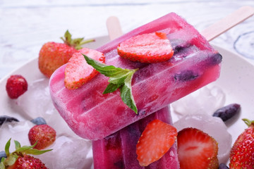 Berry popsicles with pieces of strawberry and honeysuckle on the white plate