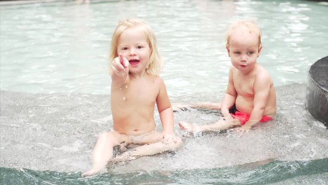 Portrait of two adorable caucasian children - boy and girl - sitting in the swimming pool and smiling
