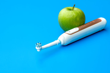 Dentist Concept green apple and modern electric toothbrush with bluetooth and mobile app over blue background.- Image