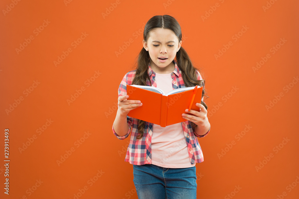 Wall mural shes a true bookworm. adorable small child reading book on orange background. cute little girl readi