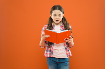 Shes a true bookworm. Adorable small child reading book on orange background. Cute little girl reading for fun. Developing reading ability in school age children. Reading comprehension and fluency - obrazy, fototapety, plakaty