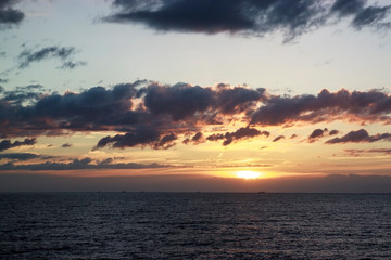 Fototapeta premium Scenic sunset over the sea. The sun sets on the water. Clouded sky is painted with bright colors. Sunset beach in a summer evening. Gulf of Finland, Baltic sea, Saint-Petersburg, Russia.