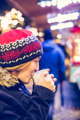 Enjoying Christmas time on the Christmas market. Young girl is drinking mulled wine.