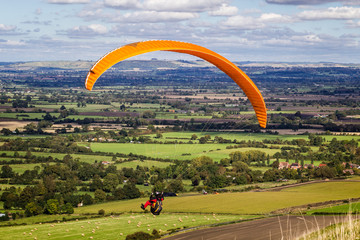 Paraglider with yellow parachute gliding over green landscape