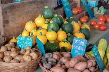 Closeup of a colorful display of fresh produce for sale at a farmer's market, with potatoes, turnips, tomatoes, squash, onions and garlic.