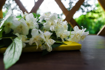 White Jasmine flowers with green leaves and yellow notebook on dark brown wooden table. Flat lay, top view, copy space for text. Floral wallpaper concept