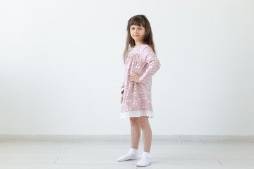 Little proud brunette girl in a pink dress is standing on a white background. The concept of stylish children's clothing and preschool age. Copyspace.
