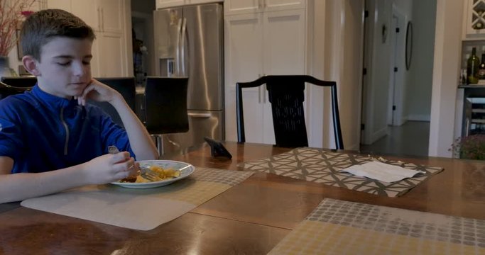 12 - 13 year old boy eating breakfast alone at a kitchen or dining room table