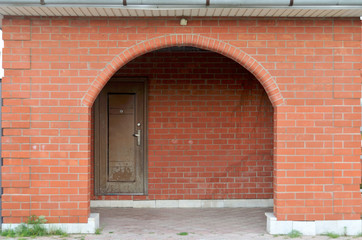 Fototapeta na wymiar Old village country house with an inviting entrance on cobblestone through a brown door set in a red arch brick wall