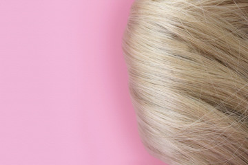 Beautiful hair. Light brown hair. Hair is gathered in a bun on a pink background. With free space for text. For a poster or business card.