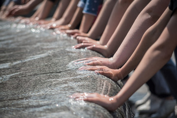 Children hold their hands in the water of the fountain