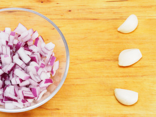 Sliced red onions in a transparent bowl and garlic cloves on a wooden background