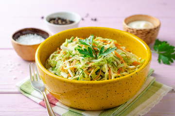 Coleslaw salad with cabbage, carrot and cucumber in bowl on purple wooden background. Selective focus.