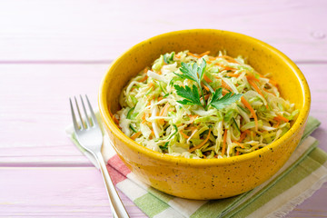 Coleslaw salad with cabbage, carrot and cucumber in bowl on purple wooden background. Selective focus.