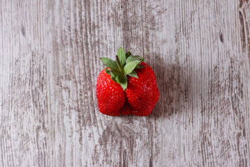 Ugly strawberry on wooden background. Trendy ugly food.