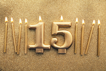 Number 15 gold celebration candle on a glitter background