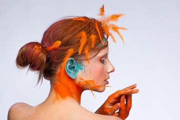 Portrait of a beautiful model with creative make-up and hairstyle using orange feathers