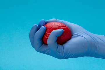 A latex glove hand squeezes a red brain. Brain treatment