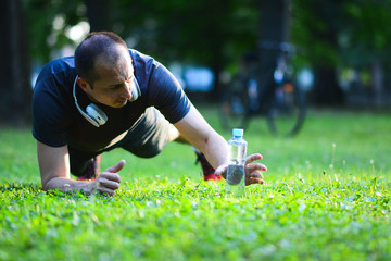 Naklejka na ściany i meble Man exercising in park. Smiling caucasian male doing core workout on grass. plastic bottle water