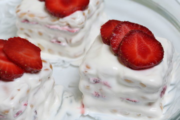 Cakes of biscuits, sour cream and strawberries. Decorated with strawberry slices. Lie on a plate.