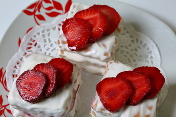 Cakes of biscuits, sour cream and strawberries. Decorated with strawberry slices. Lie on a plate.