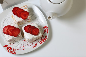 Cakes of biscuits, sour cream and strawberries. Decorated with strawberry slices. Near there is a teapot.