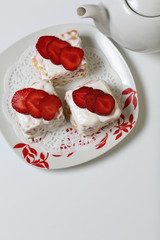 Cakes of biscuits, sour cream and strawberries. Decorated with strawberry slices. Near there is a teapot.