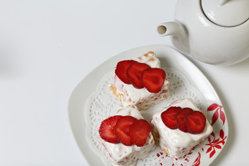 Cakes of biscuits, sour cream and strawberries. Decorated with strawberry slices. Near there is a teapot.