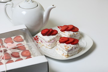 Cake from cookies, sour cream and strawberries. Decorated with strawberry slices. Near the same pastries and teapot.