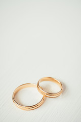 Intersecting wedding gold rings at the bottom of the white wooden background. Vertical.