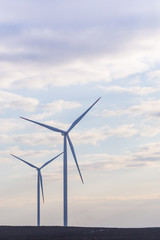 Fototapeta premium Two wind turbines on agricultural ground with cloudy sky in background