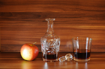 An open whiskey carafe, a glass of whiskey and an apple on a wooden table