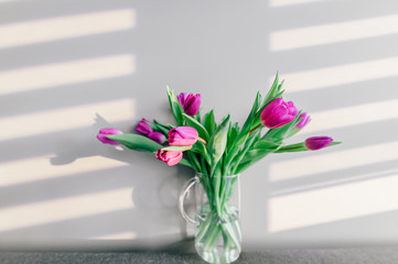 Glass vase with bouquet of beautiful tulips on grey wall background.