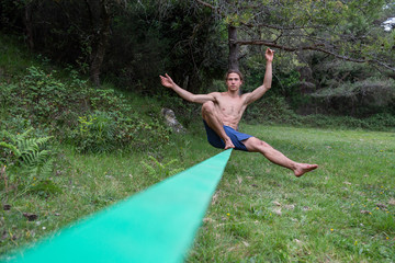 Active young man with naked torso balancing on slackline in green field on summertime