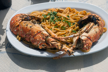 Delicious lunch by the sea. A white plate of spaghetti with huge lobsters on the grill. Travel to Santorini, Greece. Old port of Fira.